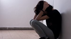 Girl holding her head and crouching down because she hates herself. What to do when you hate yourself from TheHopeLIne