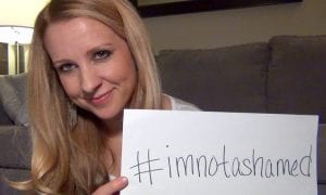 Woman holding up piece of paper that reads #imnotashamed